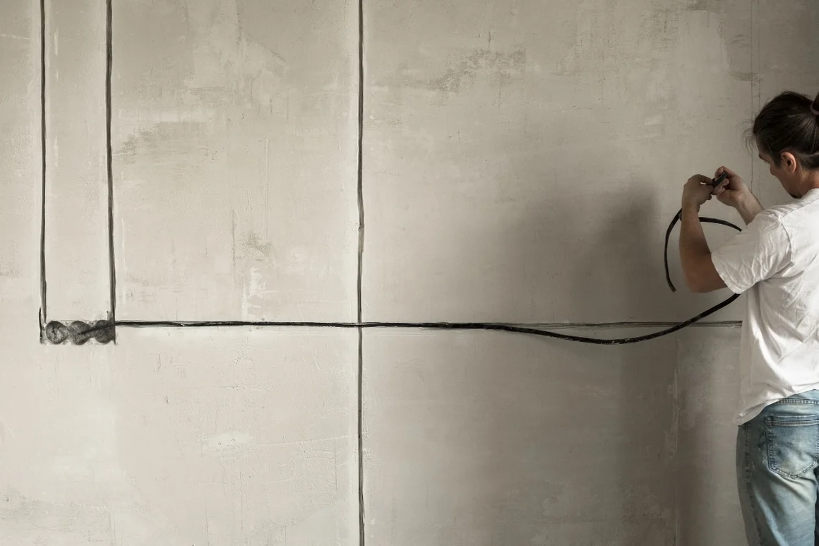 Person verlegt Stromkabel an Wand